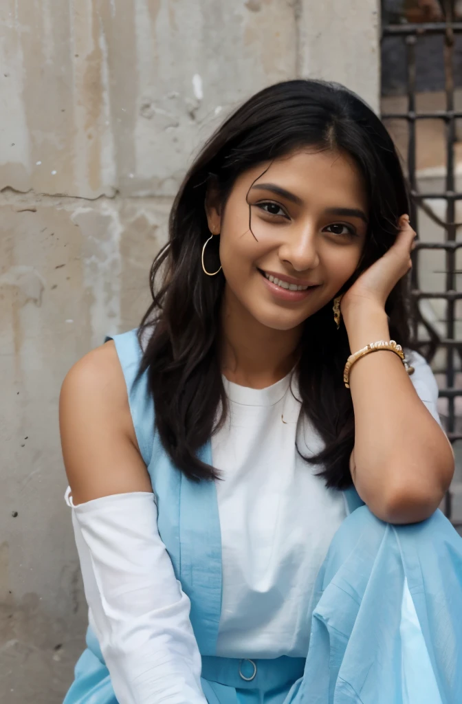 an Indian girl with honey color skin tone, black soft and silky hair till shoulders, wearing a light blue salwar with white borders and white chunni, she is wearing earrings, wearing 2 light colored bangles on each hand, wearing this spectacles, smiling white teeth, rose color lips, happy and excited, pink nail polish, tilting right as if she is talking to someone sitting on the ground slowly, left hand on her left knee, other hand pushing her open hairs behind her right ear revealing a nice earring, realistic, background has walls, on her left is a low wall with pointy fence, behind her is a metal gate and a wall with a ledge to keep flower pots, its evening time, hyper realistic, wide shot, girl is smiling, showing teeth, full body visible