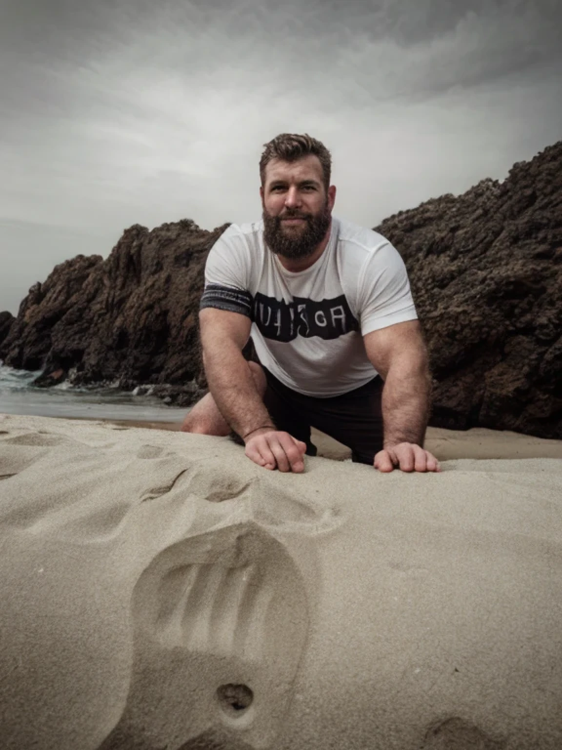 Wide angle, macho hairy beefy handsome man wearing a loose t-shirt, black and white photography, photorealism, canon photography, award winning photo, well built arms, on the beach, by John Singer Sargent, james gurney, justin gerard, john william waterhouse, highly detailed, artstation,