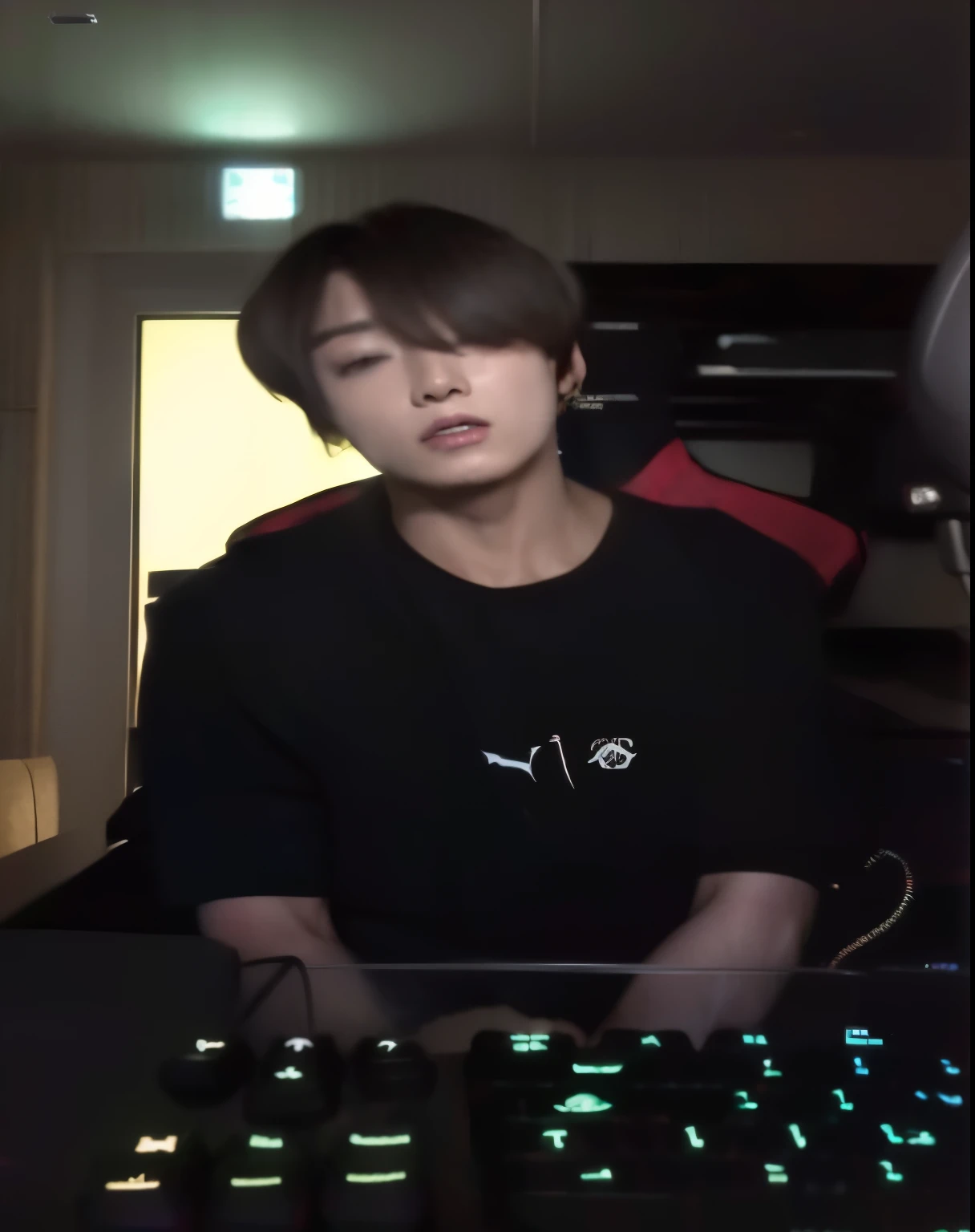 There is a man sitting at a computer desk with a gaming keyboard, Jungkook gamer, Jungkook face, he is wearing a black rock t-shirt, jovem bts, Jungkook,