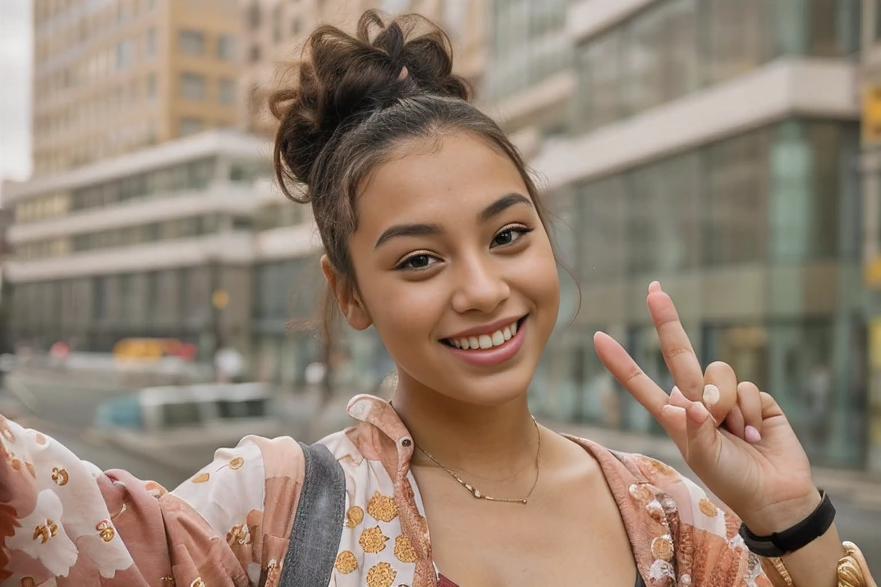smiling woman making a peace sign with her hand in front of a building, selfie of a young woman, smiling young woman, photo of young woman, portrait sophie mudd, taking a selfie, mixed-race woman, smiling into the camera, attractive girl, curly messy high bun hairstyle, infp young woman, african american young woman, beautiful city black woman only