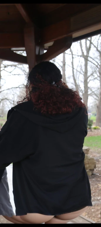 there are two people standing under a shelter talking to each other, photo still of behind view, shot from the back, view from the back, seen from the back, back of the hair, from the back, wearing a black hoodie, with curly red hair, facing away from camera, long dark curly hair, over the shoulder view, in a black hoodie, beautiful girl, big ass, huge ass, bbw, from behind, thick, thick thighs, wide hips, bbw, big tits, sideboob, giant ass, back view, big butt, round butt, tight underwear, underwear halfway off, underwear taking off, grabbing ass, ass spilling over underwear, too thick for clothes, looking left, leftwards, latina, from behind