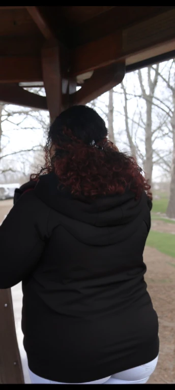 there are two people standing under a shelter talking to each other, photo still of behind view, shot from the back, view from the back, seen from the back, back of the hair, from the back, wearing a black hoodie, with curly red hair, facing away from camera, long dark curly hair, over the shoulder view, in a black hoodie, beautiful girl, big ass, huge ass, bbw, from behind, thick, thick thighs, wide hips, bbw, big tits, sideboob, giant ass, back view, big butt, round butt, tight underwear, underwear halfway off, underwear taking off, grabbing ass, ass spilling over underwear, too thick for clothes, looking left, leftwards, latina, from behind