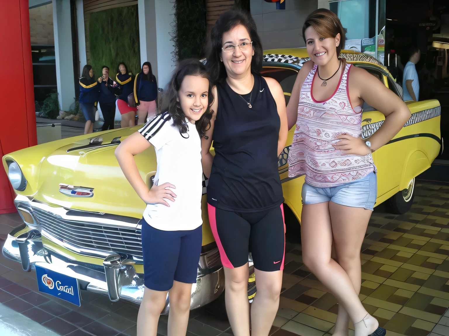 three women next to a yellow car in a building, in front of a lowrider. A woman with tanned white skin and dark hair. She is about 35 years old. Her slightly plump lips are like a delicate flower, her dark brown eyes seem to contain a world of wonders. Slim body. Thin waist. Her body exudes glamor and her face is the definition of beauty. Test, highly realistic, reddish skin, beautiful, soft lips, pink lipstick, smiling, feeling of lightness and joy, hyperrealism, very elaborate skin, direct look. Woman in good physical shape, full body photo, clear photo, high quality, high resolution, masterpiece, 8K.