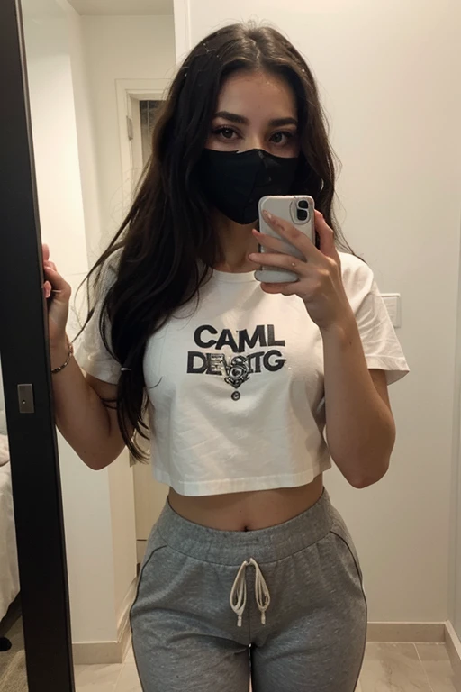 Chica sexy de pelo largo y negro con camisa negra  y joggers grises tomandose una selfie agachada frente al espejo, con mascarilla negra