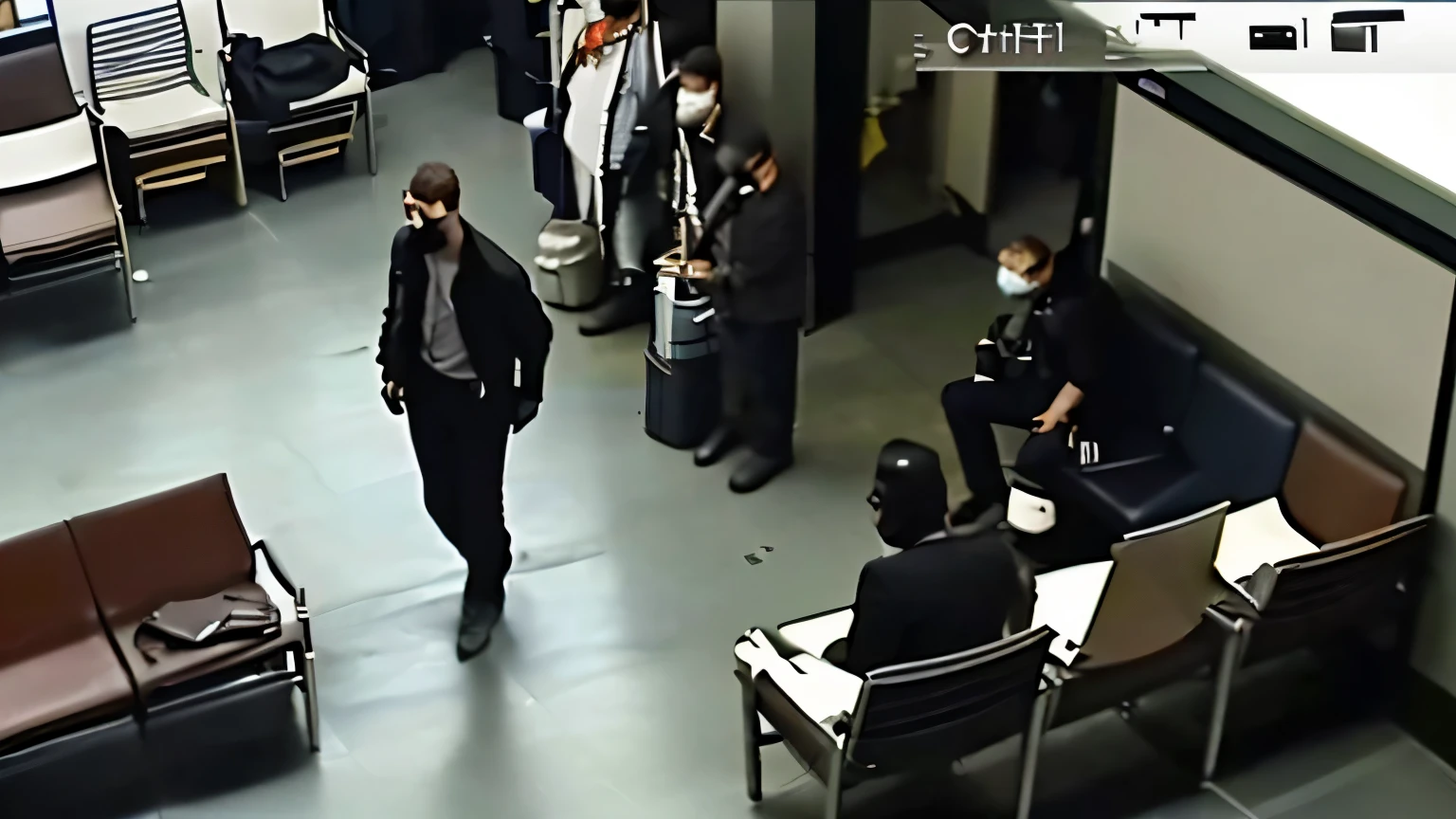 A man is walking with a shirt inside a black jacket and wearing sunglasses. He is not in the center. (Side view.) ((((Screenshot from a surveillance camera in an airport waiting room. People are sparse. Somewhat rough image quality but high quality. This was taken from diagonally above.)))
