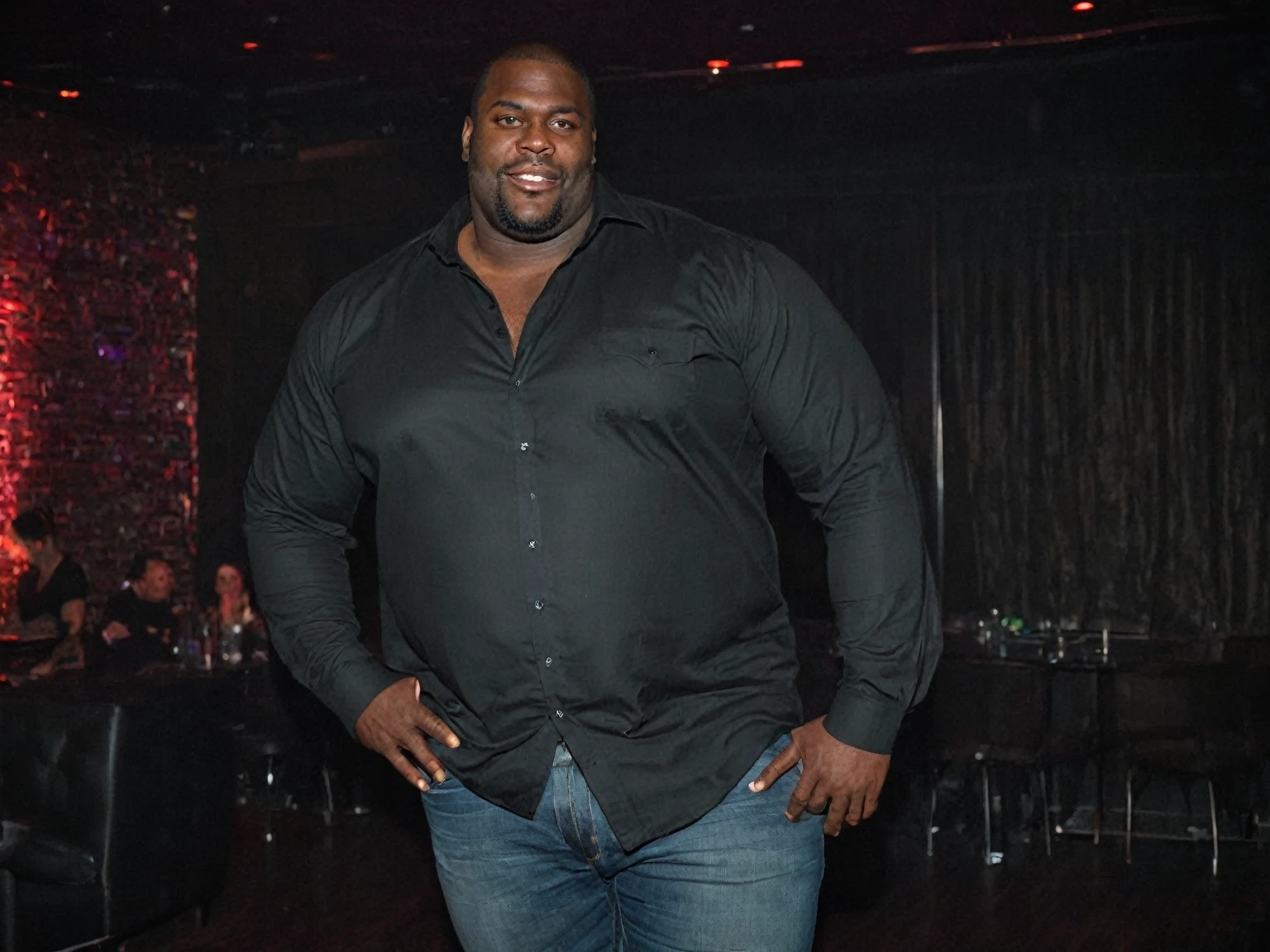 A full body picture of a massive, muscular, strong, giant, tall, wide black man, 39 years old, wearing long-sleeved, button-up, black shirt and jeans, lustful, in a nightclub
