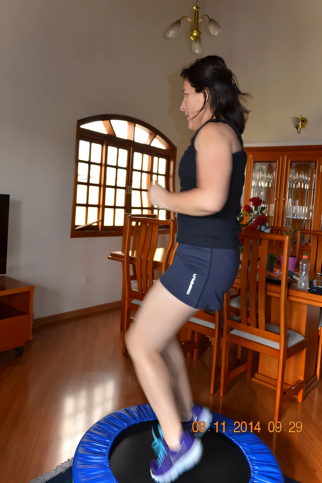 woman jumping on a trampol in a living room with a dining room table, indoor, jumping, working out, indoor shot, not blurry, cottagecore!! fitness body, shot on nikon d 3200, side view of her taking steps. She is about 35 years old. Full body photo, clear photo, high quality, high resolution, masterpiece, 8K