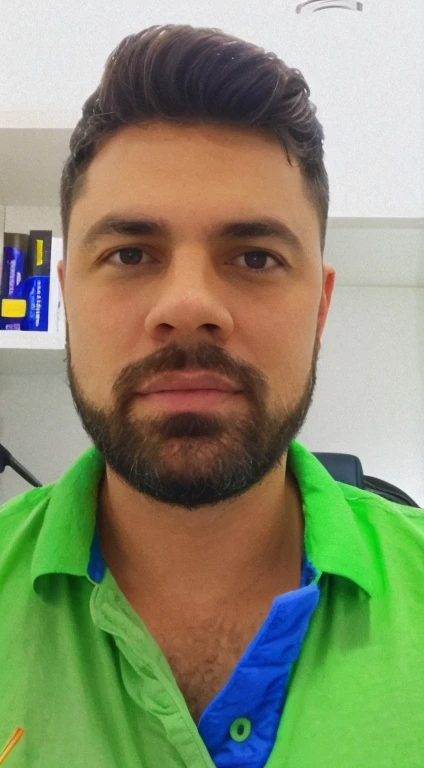 There is a man with a beard and a green shirt, frontal photo, with a desk in the background.