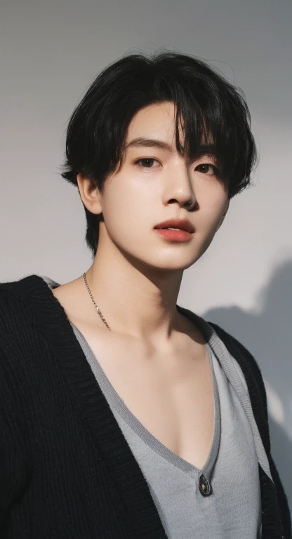 male in black cardigan oversize, collar bone, grey wall background, shadow in background, handsome boy\'s plump lips, round face shape, black hair, black korean hairstyle, silver neckclase, iphone lens, detailed, realistic
