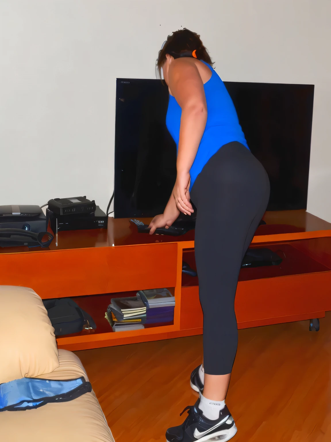 woman in blue shirt and black leggings standing in front of a tv, bending over, somewhat bent over, bent over posture, bent over, bent - over posture, bend over posture, toned derriere, black leggins, tight attire, black leggings, black spandex, side view of her taking steps, wearing black tight clothing, leggins, side shot