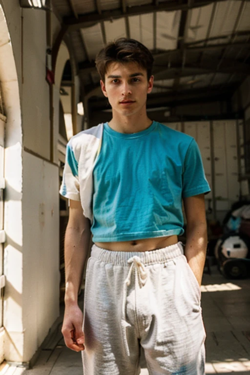 Un homme twink mignon de 19 ans d'1m74 assez fin. Il porte un t-shirt multicolore très ample en boule et se cache derrière un mur dans un hangar. Il a le regard apeuré. There is a light from the sunset reflecting on his skin.