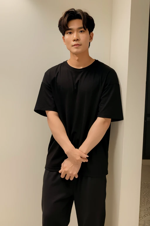A Thai man wearing an oversized black T-shirt with no pattern leans against a wall.