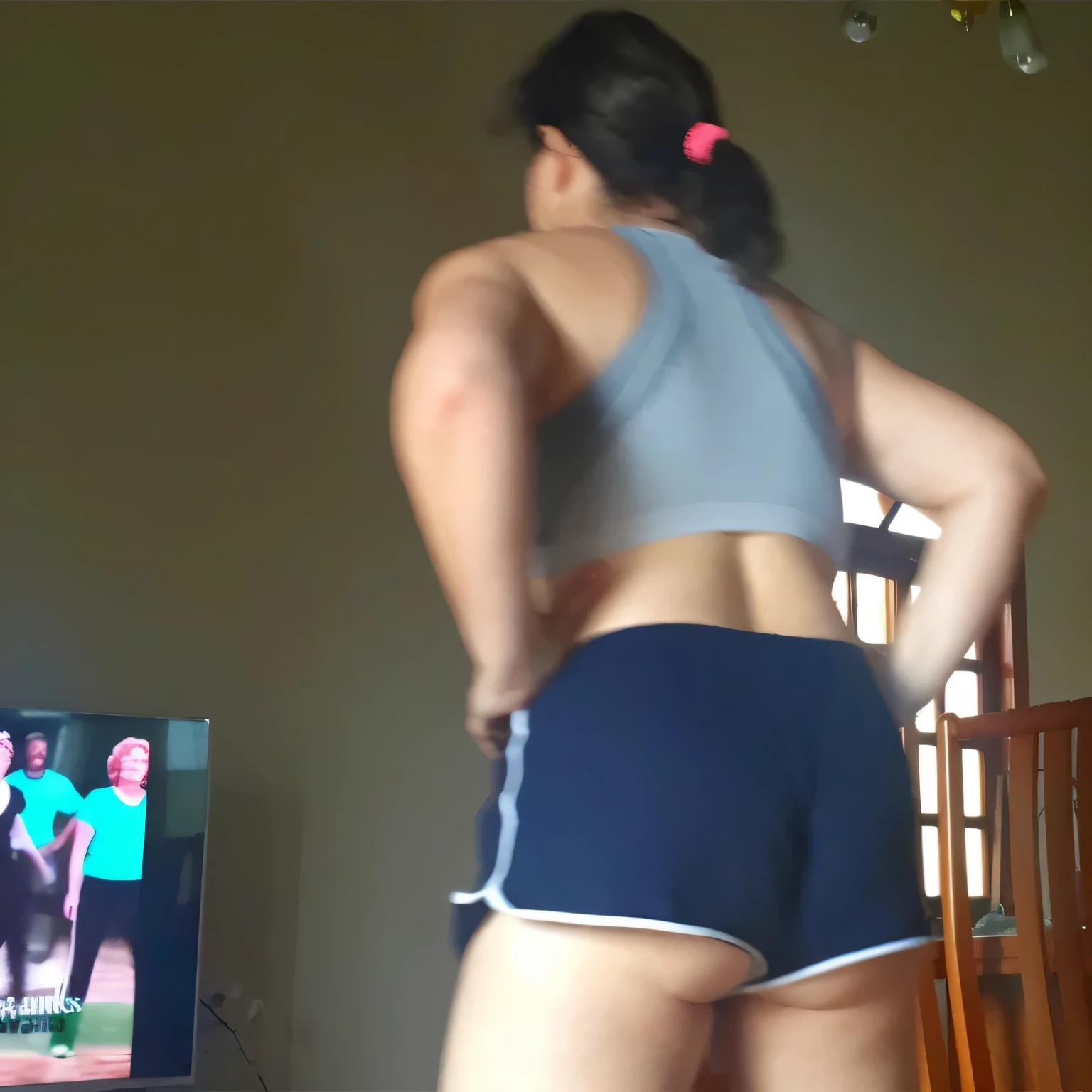 A woman is in the living room, dancing in front of a television, with her back to the camera, hands on her hips. She is wearing a gray top and very short black shorts. Beautiful woman, extremely sexy, very sensual. (ultra quality masterpiece) with toned body, 35 years old, 1.62 tall, 60 kg, best quality, perfect face, perfect mouth, perfect hands, (((black hair))), is standing, ( full body) wearing a tank top, very short black shorts (((short black shorts)))), dark brown hair, short black shorts for gym training, well defined. Tanned body, sexy pose, shapely and well-defined legs, high contrast, Ultra HD, 16K. Photorealistic, detailed and realistic hands, 5 fingers per hand, dark hair, full body photo, clear and high quality photo. Masterpiece: 1.3, high resolution, (photographically realistic), 8k, NUDE, NUDITY, NFSW.