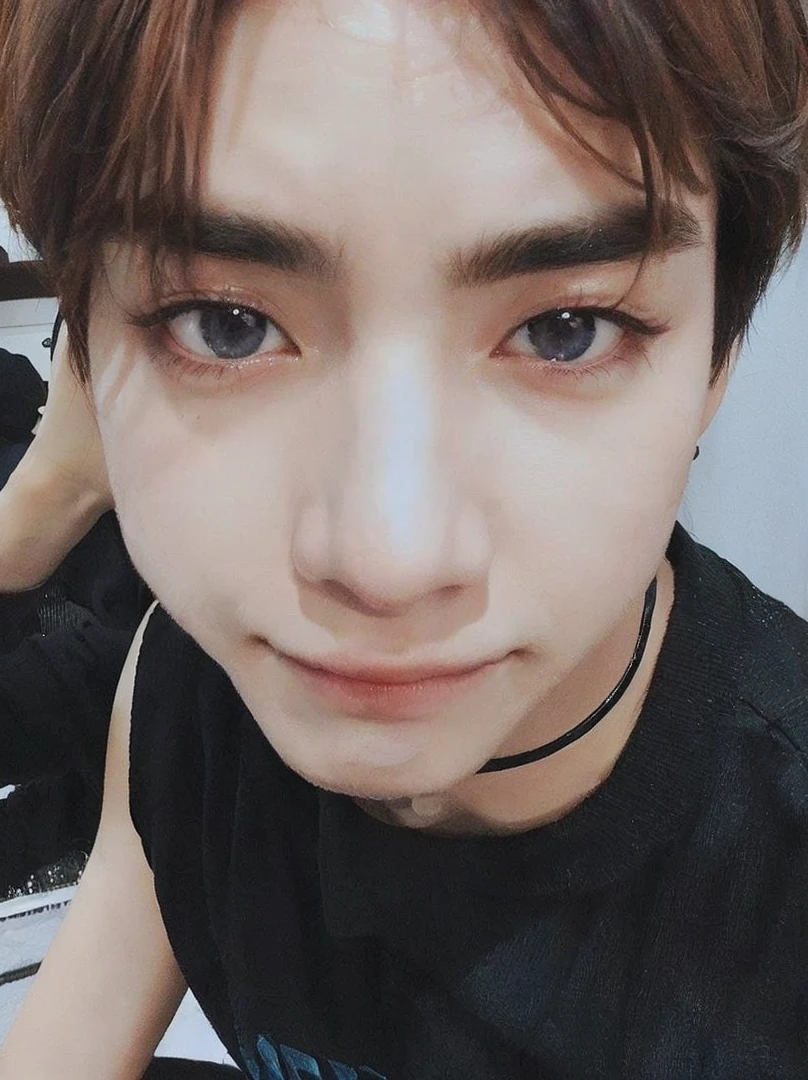 hay un joven con camisa negra y corbata, Jung Jaehyun, Jimin\his right eyelid is swollen, sus ojos parecen sabios, parece un minion humano, ojos holgados, lindos ojos redondos e inclinados, enormes ojos inclinados hacia abajo, pale korean adorable face, pupilas hendidas, sus ojos son rojos y brillantes