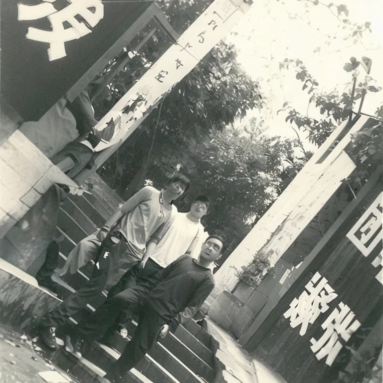 Three young men from mainland China took a group photo standing in front of the stairs，Behind are building pillars, slogans and some trees，Black and white photo，high resolution,Best quality，masterpiece，超high resolution，（Honesty：1.4），RAW photos
