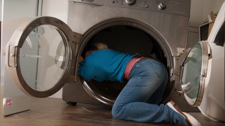 brunette ssbbw wearing leggings and a hoodie with glasses and a baseball cap stuck in the washing machine