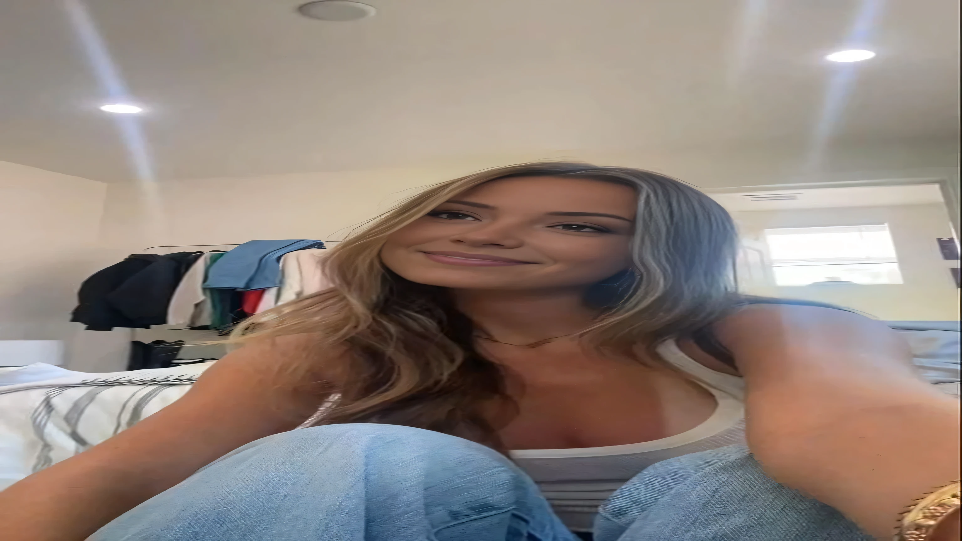 arafed woman sitting on a bed with a white tank top, He nods his head, posant dans une chambre, she is facing the camera, belle et souriante, Portrait de Sophie Mudd, Kailee Mandel, photo de profil, looking to the side of the camera, avoir l&#39;air mignon, regard sexy devant la caméra, regardant directement la caméra, souriant joyeusement à la caméra