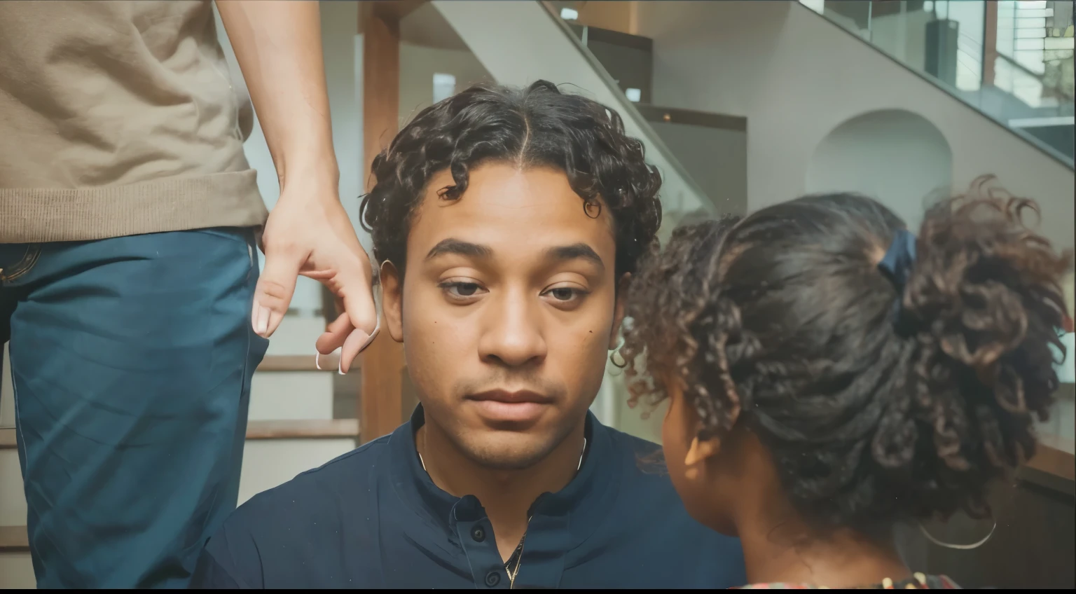 Imagine a scene where father & daughter are sharing a moment. The foreground features a little black girl with curly afro hair, dressed in a green sweater adorned with a festive red pattern. Her father face is the only one visible a black man with woolly curly-hair appearing to be in his early-50s plus, clad in a navy blue collared shirt. The little black girl stand with her back the only thing visible, facing towards the second individual. The third person arm is the only thing visible. The setting hints at an indoor environment, possibly near a staircase, as suggested by the presence of stair railings to the right. The overall mood is intimate, with a focus on the connection between the two characters.