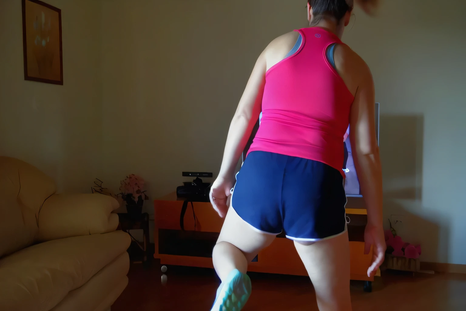 there is a woman in a pink top and blue shorts playing wii, back - shot, sport bra and shorts, long shot from back, human back legs and sneakers, sport bra and dark blue shorts, long shot from the back, shot from the back, working out, medium shot taken from behind, in shorts, rear-shot, back shot, backshot