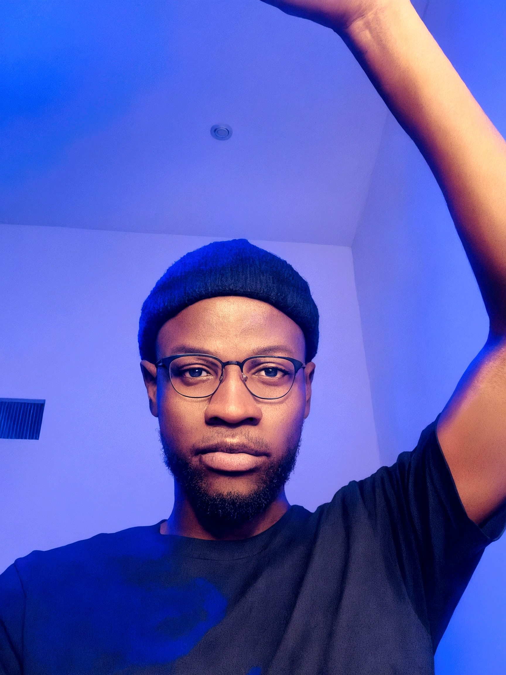 Um jovem com uma shirt preta, glasses on the face and a hat on the head, with one hand raised upwards