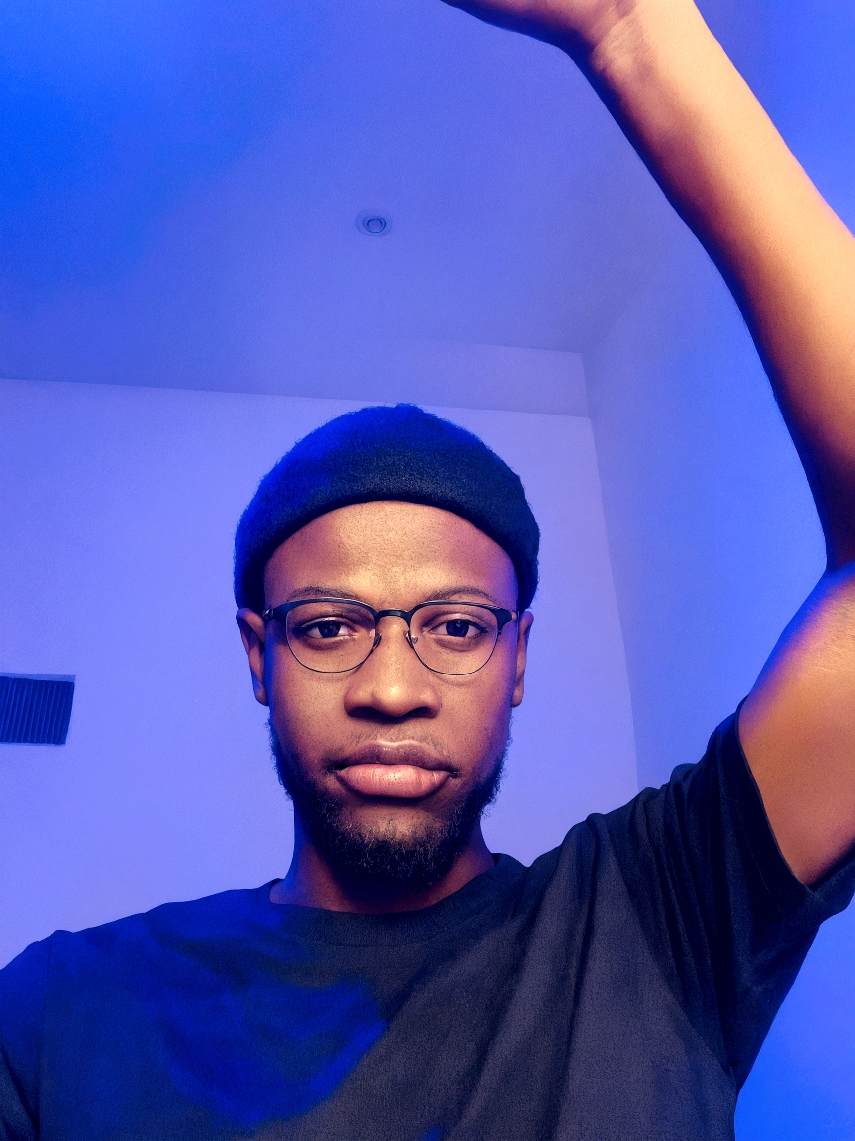 Um jovem com uma shirt preta, glasses on the face and a hat on the head, with one hand raised upwards