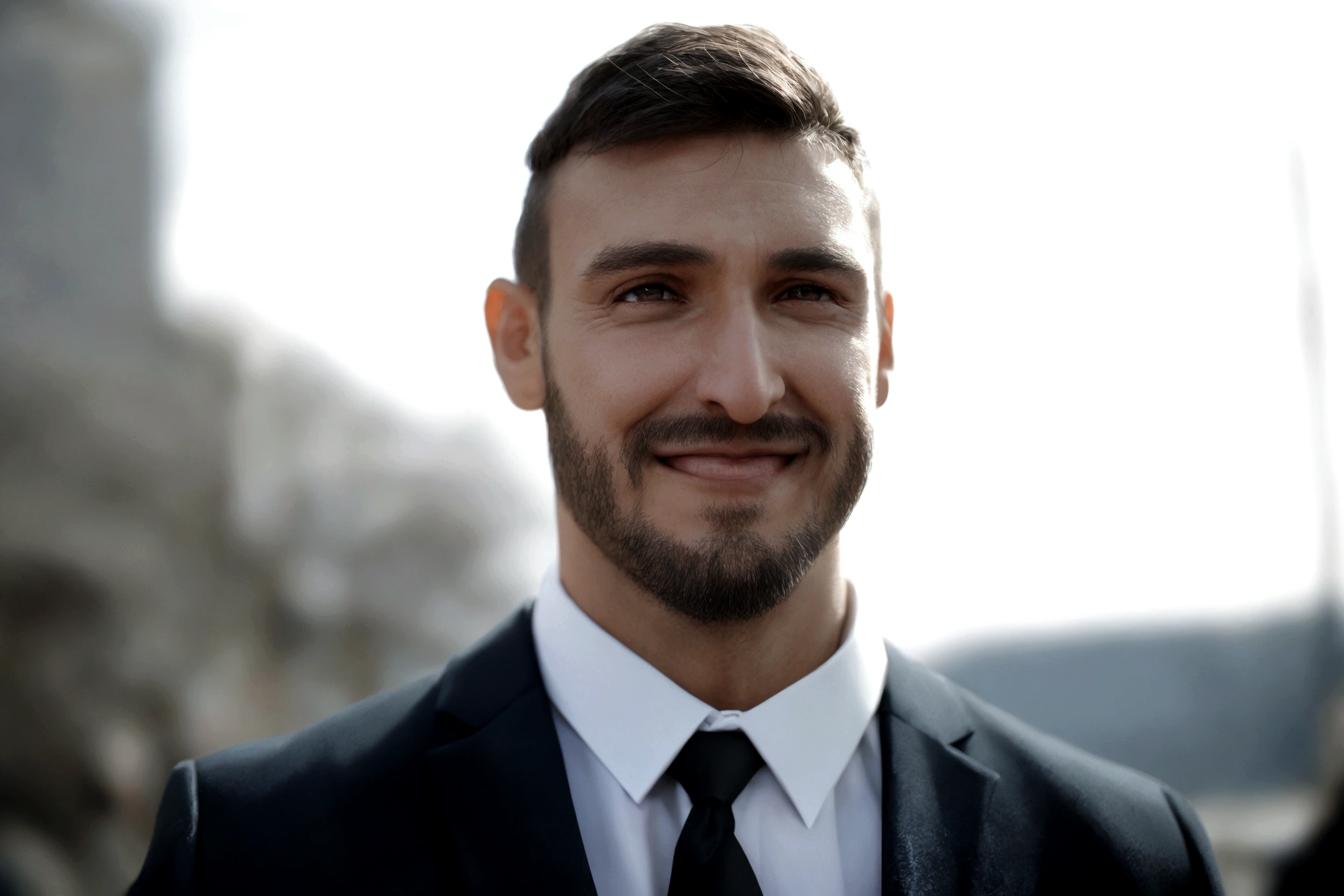 Man with a beard, smiling, in a suit and tie standing.