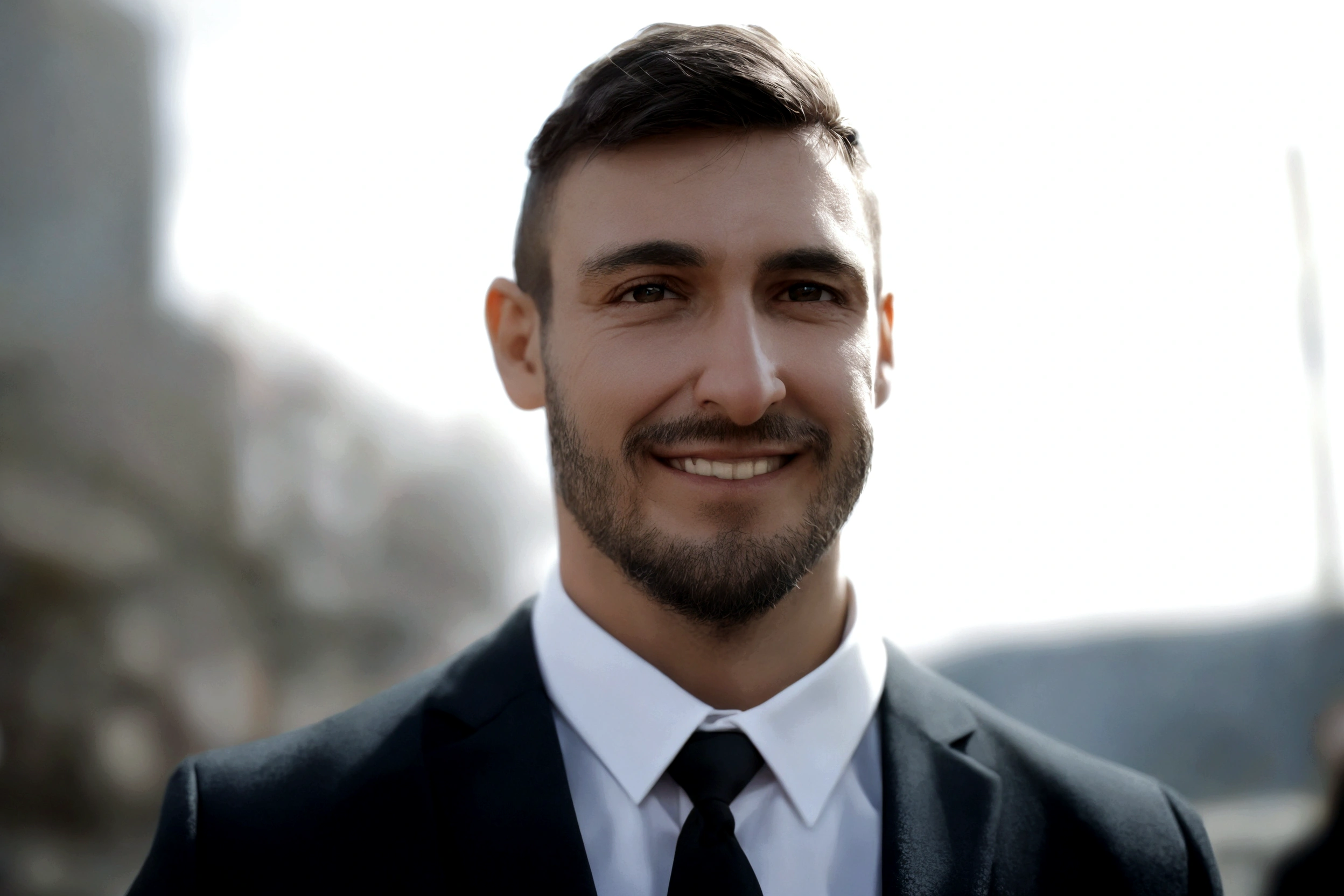 Man with a beard, smiling, in a suit and tie standing.