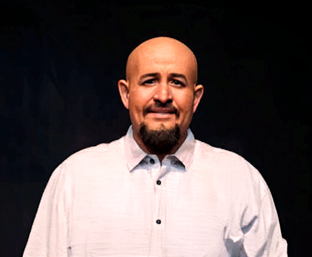 Disney Pixar style animation, faithful to the photo of a 45-year-old Brazilian man, bald, wearing a black blazer and white button-down shirt, he has a goatee and has his arms crossed