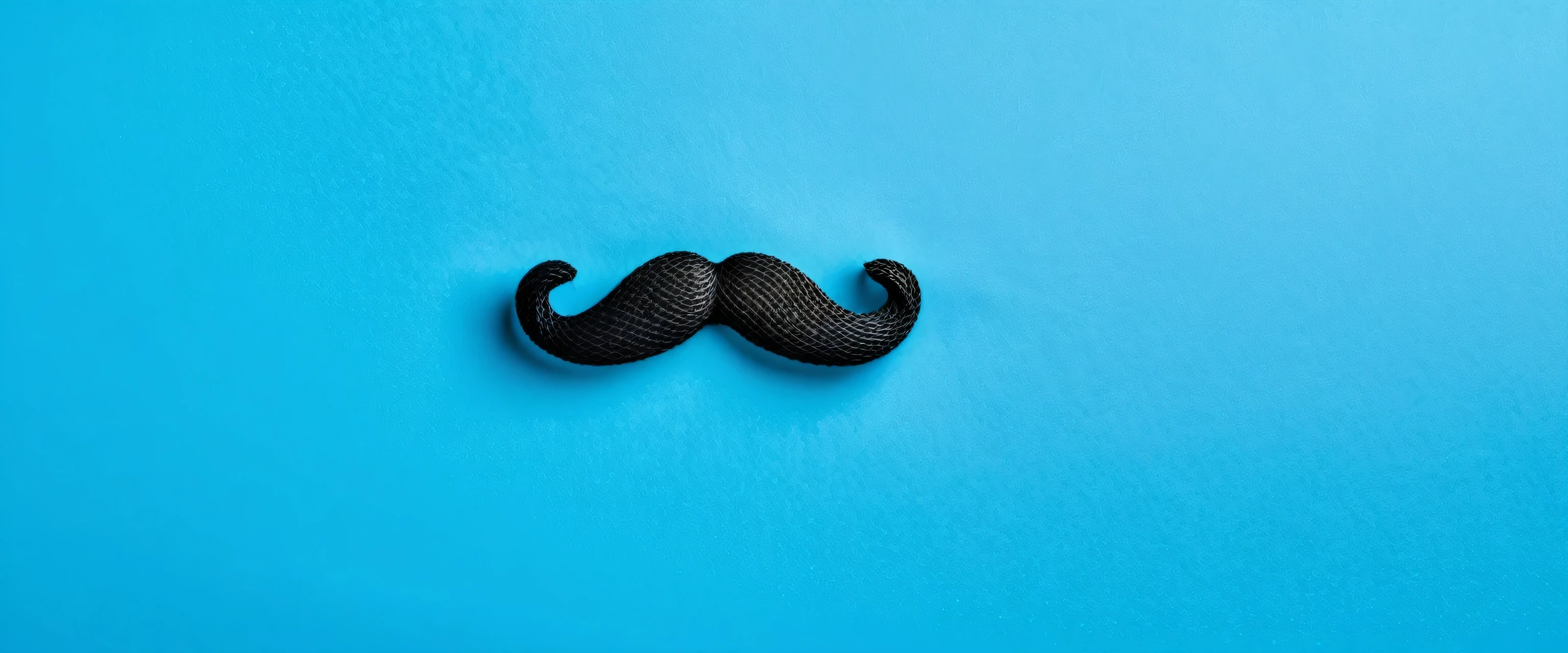 Black moustache on blue background with copy space. Movember campaign symbol. Prostate cancer awareness month.