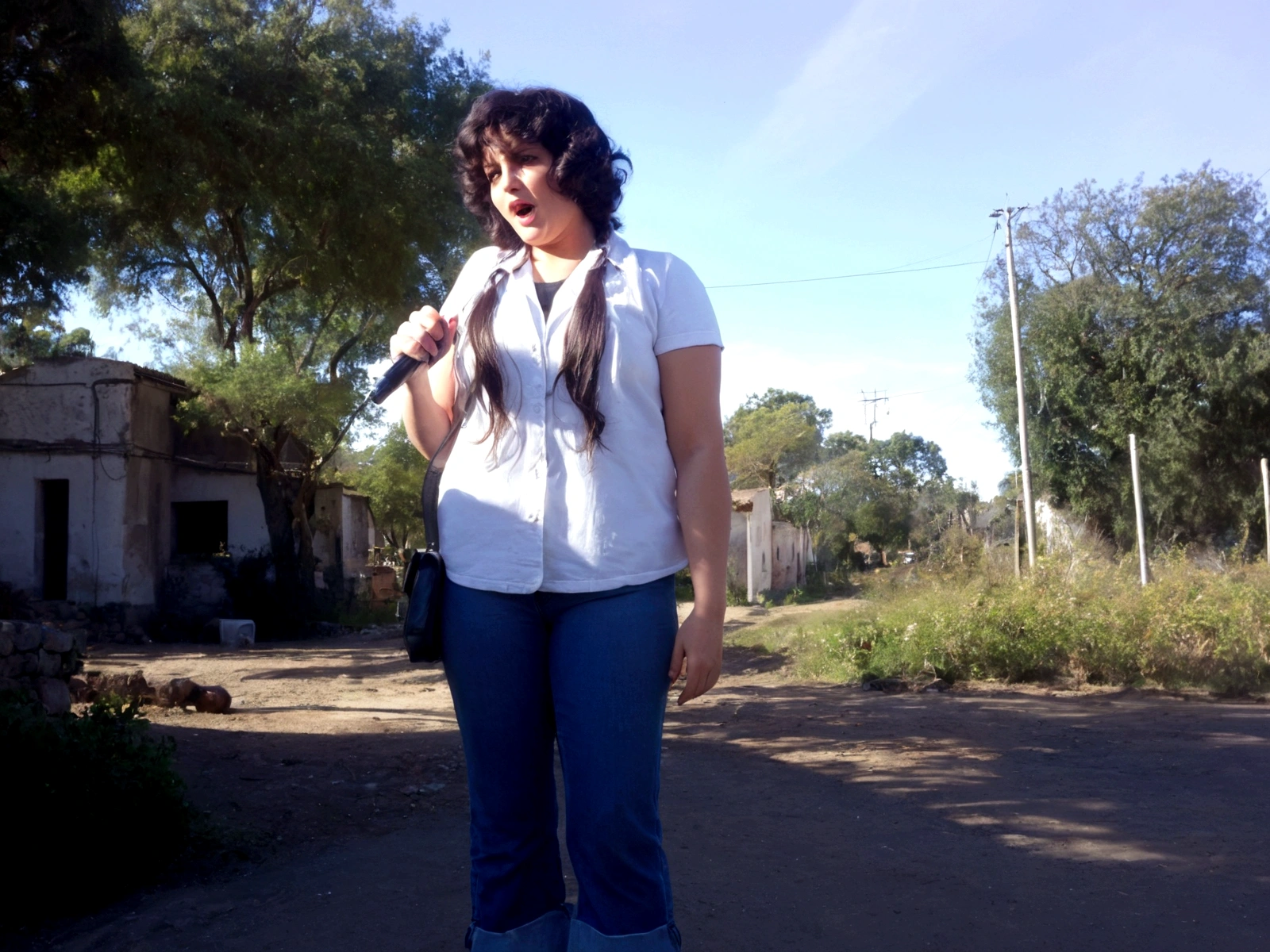 mujer cantando, vestida de chaqueta de jeans, remera blanca larga hasta los muslos, Oxford-style jeans from the 70s, cabello ondulado, recojido, con audifinos de vimvha, holding an old microphone from the 1940s, fondo de pradera, con pastos verdes, florores,