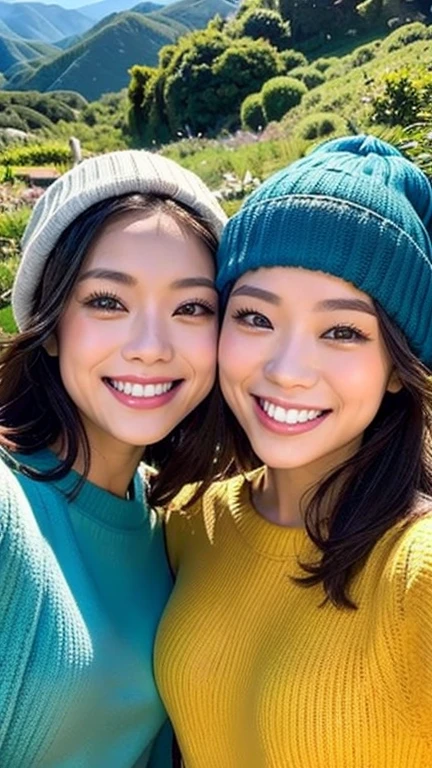 "Two women taking a selfie with a mountainous landscape in the background. One is wearing a blue beanie and the other is wearing a yellow beanie. Both are smiling brightly and wearing long-sleeve sweaters. Sunlight illuminates their faces, and the background features lush green trees and distant mountains under a clear sky, creating a beautiful scenic view."