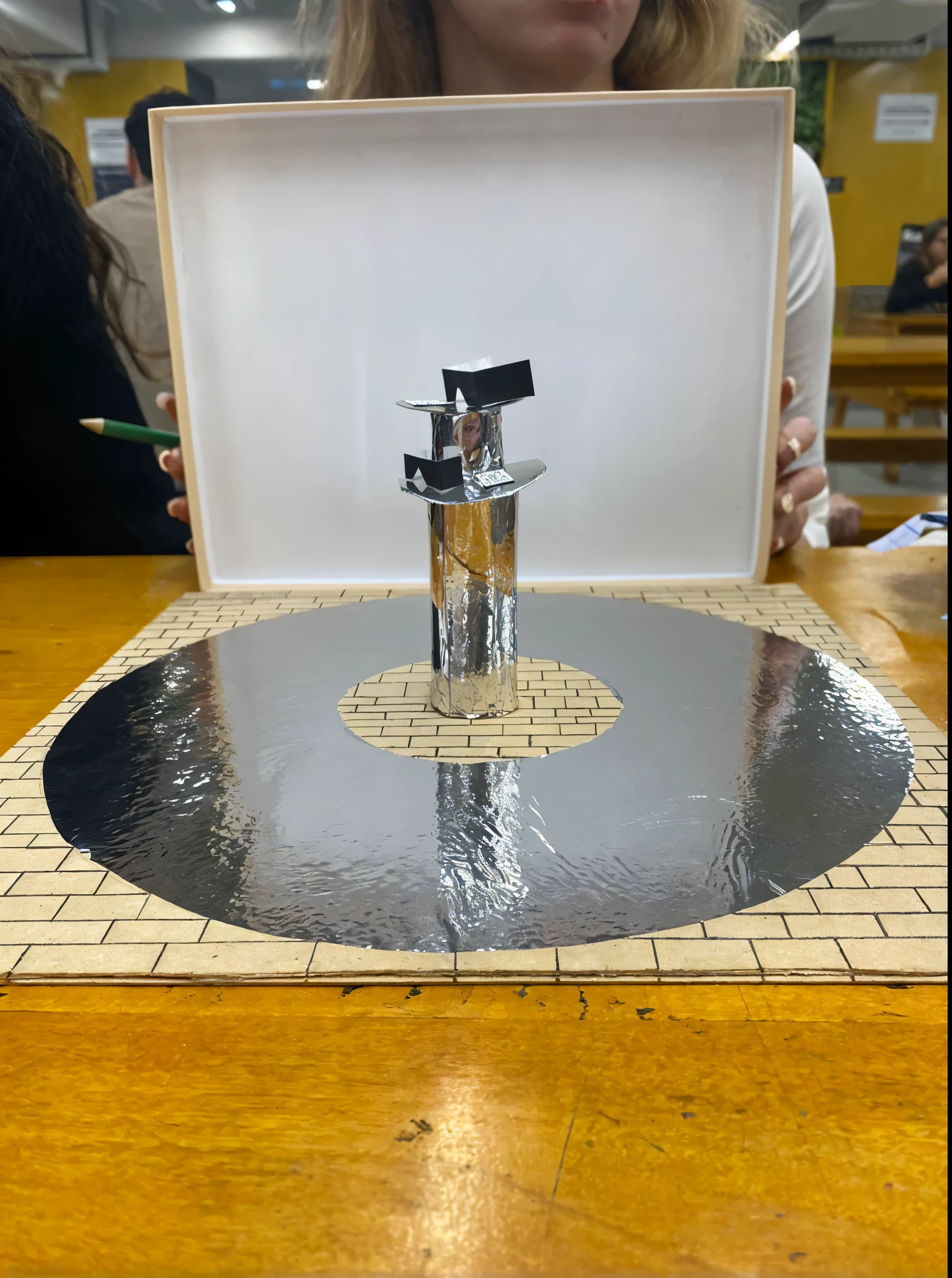 genere un boceto de una maqueta de una inatalacion realizada en un patio con piso gris. It is a circle like a ring of mirrored material attached to the floor and the middle has a small, mirrored circular structure that holds and presents two virtual reality lenses.