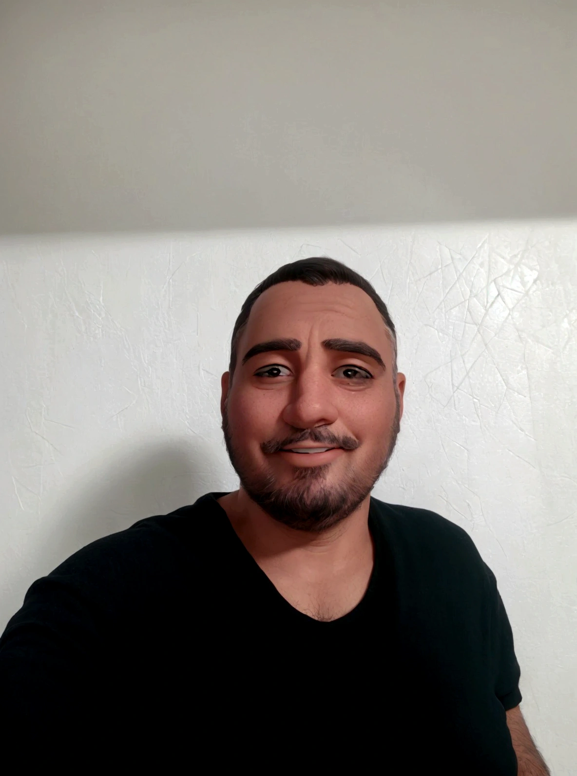 man with short black beard sitting at the table in his home holding his cell phone and smiling