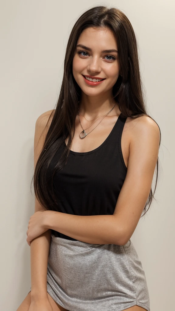 A young woman with long dark hair is smiling at the camera. She is wearing a black tank top and a silver necklace with a sun pendant. Her hair is pulled back and she has a light complexion. She is looking at the camera with a warm, friendly smile. The background of the image is a white wall.