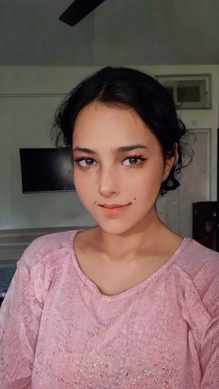 A young woman with a pink shirt and black hair is standing in front of a monitor or TV screen. The woman appears to be in her early twenties and has a feminine appearance. The photo also includes a picture or frame hanging on the wall in the background. The woman''s face is the main focus of the image, with her pink shirt standing out against the dark background. She has a neutral expression, with her eyes and mouth clearly visible. The overall color scheme of the image includes shades of pink, black, and brown.
