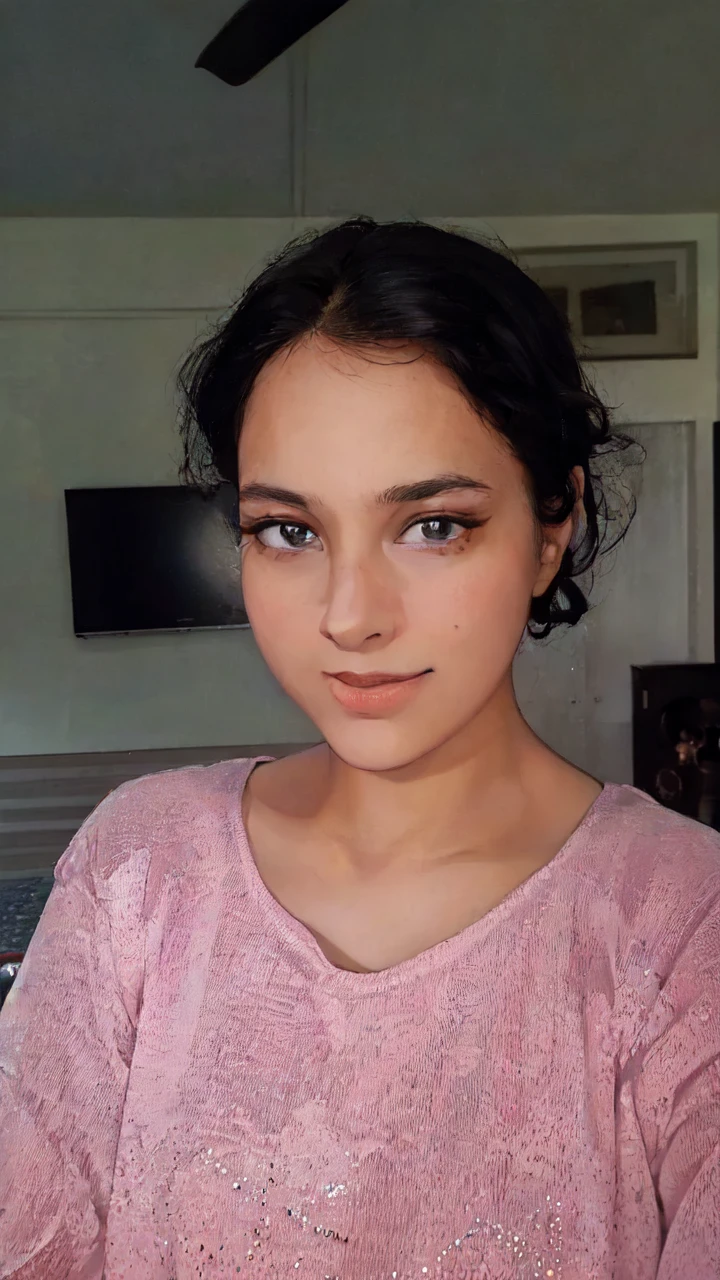 A young woman with a pink shirt and black hair is standing in front of a monitor or TV screen. The woman appears to be in her early twenties and has a feminine appearance. The photo also includes a picture or frame hanging on the wall in the background. The woman''s face is the main focus of the image, with her pink shirt standing out against the dark background. She has a neutral expression, with her eyes and mouth clearly visible. The overall color scheme of the image includes shades of pink, black, and brown.