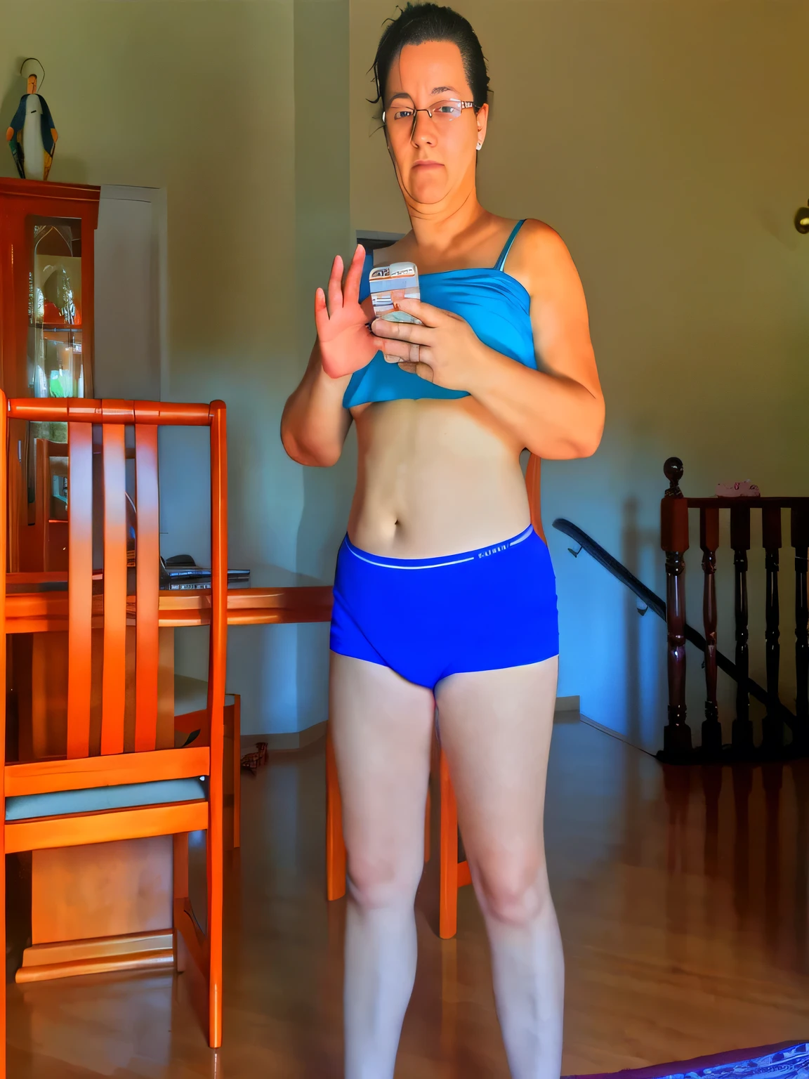 there is a woman in a blue top and blue shorts holding a cell phone, sport bra and dark blue shorts, (45 years old), 40 years woman, sport bra and shorts, short robust woman, physical : tinyest midriff ever, wearing a camisole and shorts, half body cropping, she is about 40 years old