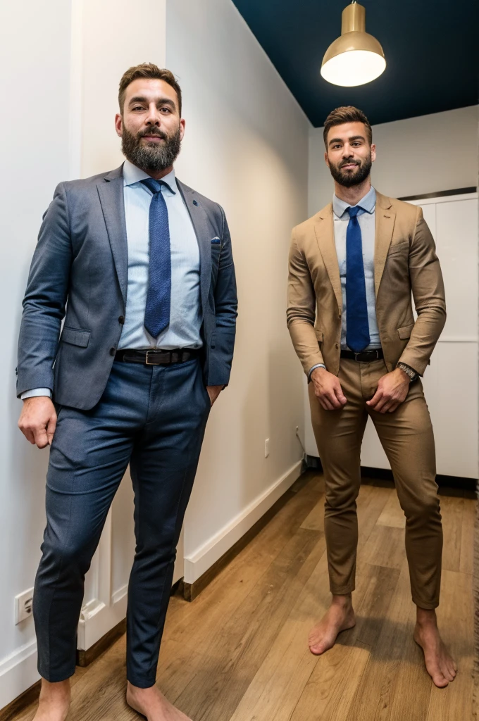 Two Italian men stand barefoot in an office, both dressed stylishly and sporting well-groomed beards. The man on the left is very tall, his head almost touching the ceiling, and wears a suit with a tie, with one hand in his pocket. The man on the right, much shorter and wearing a shirt, faces the taller man, looking directly at his chest. The height difference between them is strikingly large.