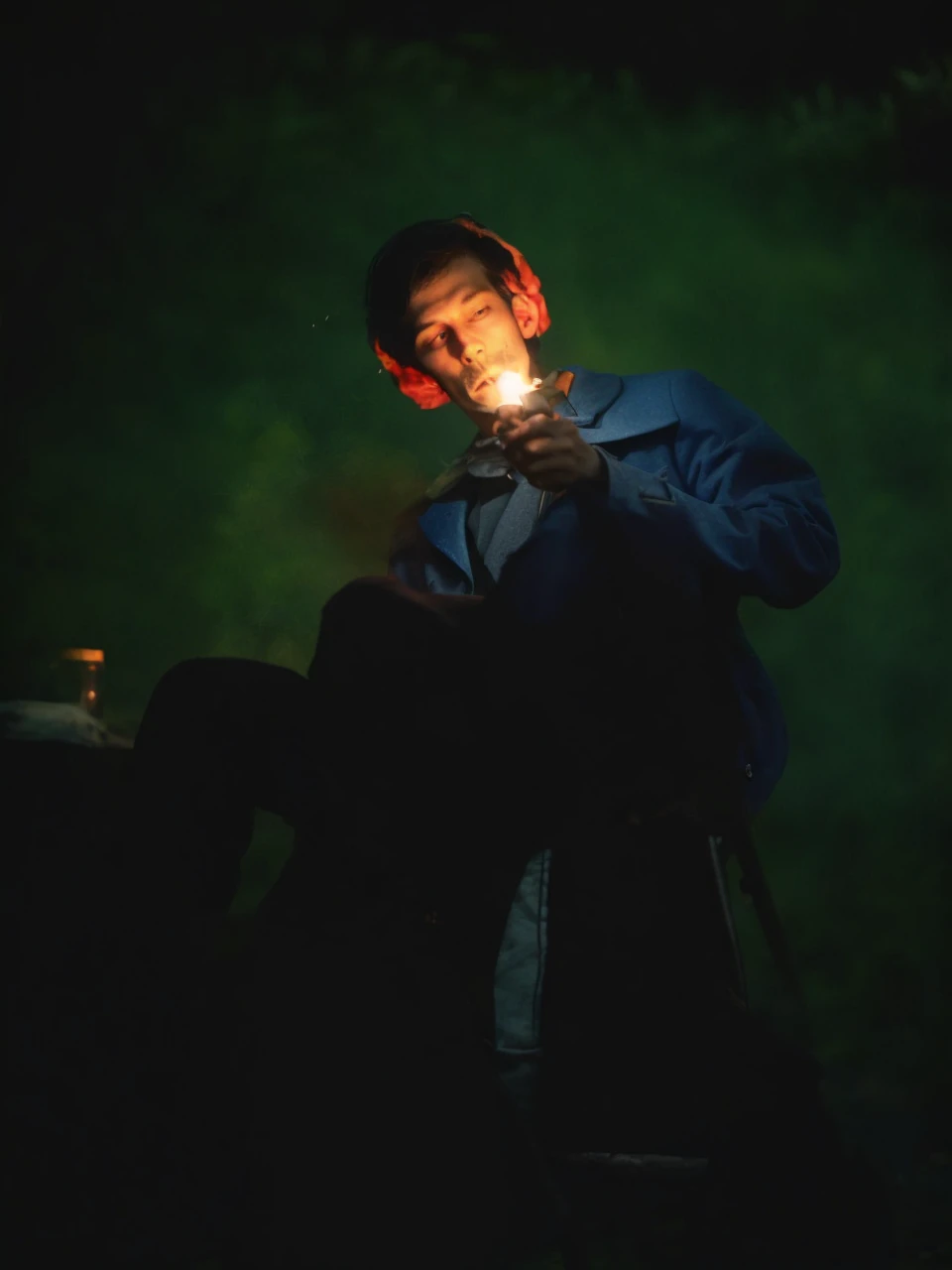Man, skin melting, lighting cigarette, old chair, tree behind, dark forest background, image in dim light, torn blue coat, black pants with chain, combat boots, penetrating gaze, lit by torches,
