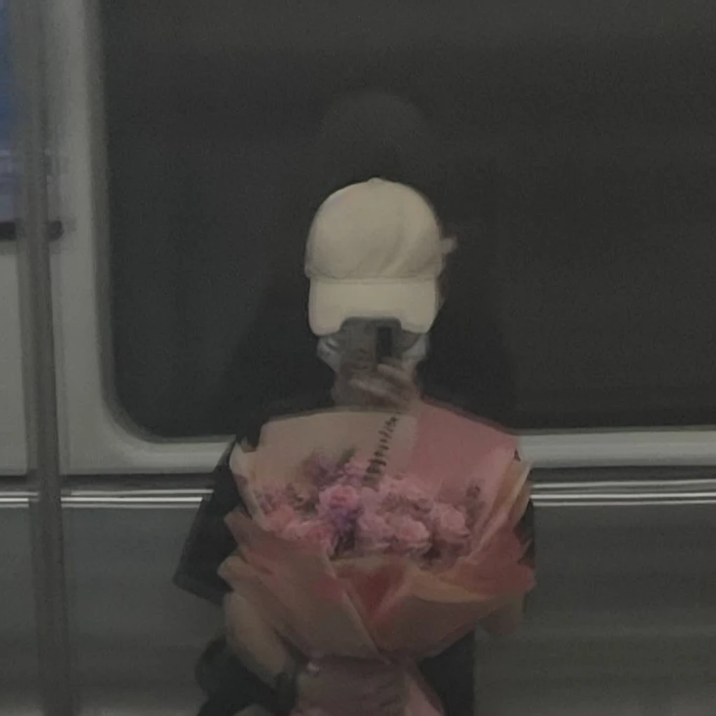 Prompt:

"Reflection of a person on a subway window, holding a bouquet of pink flowers. The person is wearing a white cap and a black outfit, partially obscured by the reflection and dim lighting. The background shows a blurred, dark subway interior, giving a moody and introspective ambiance. The bouquet is wrapped in pink paper, adding a soft, delicate contrast to the otherwise dark and muted tones of the scene."

Detailed Breakdown:

Setting: Subway window with reflection, dark interior.
Subject: Person holding a bouquet, wearing a white cap and black outfit.
Lighting: Dim, moody, emphasizing the reflective surface.
Colors: Dark tones with a pop of pink from the flowers.
Mood: Introspective, calm, and somewhat melancholic.
Use these details to guide the stable diffusion model in creating an image with a similar vibe and composition.