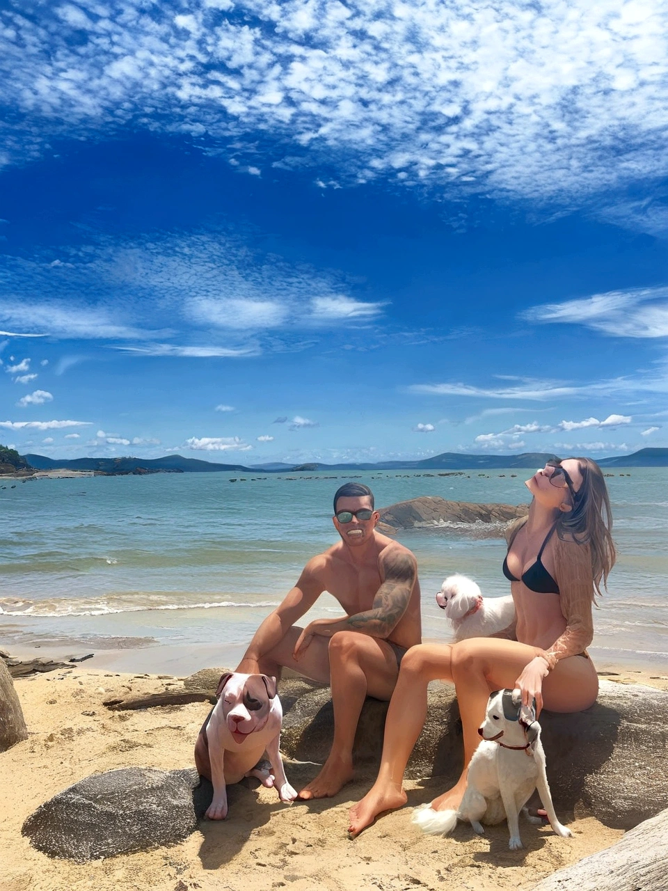 young couple sitting by the sea with 3 dogs, a pitbull, a poodle and a pischer