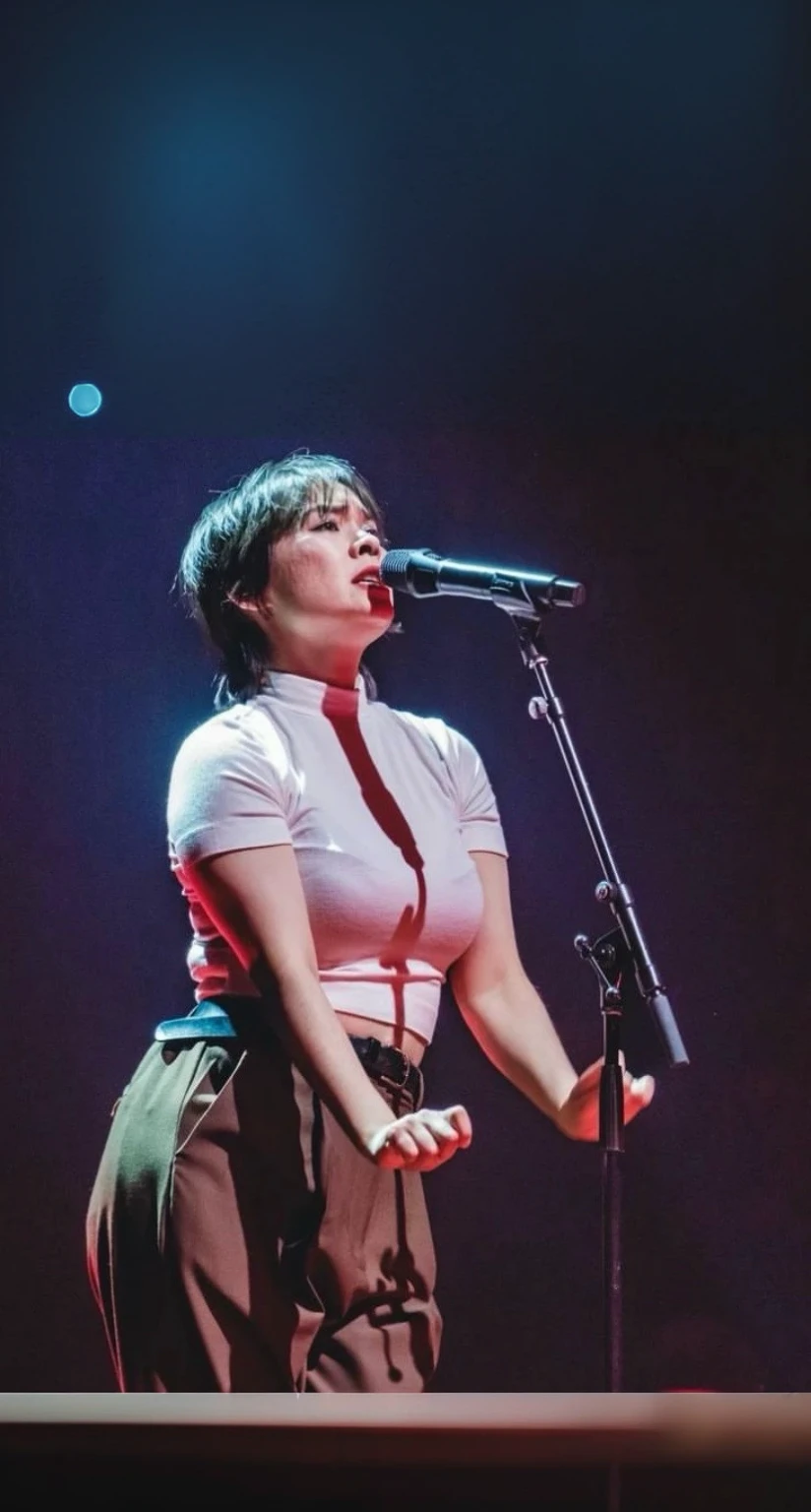Dark background with cold blueish light falling onto the woman; dark brown pants and microphone
