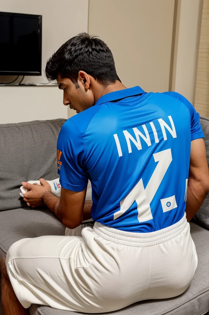 In the room a 18 year old boy is sitting on the sofa and watching the television. He has were the India cricket team jersey and on his jersey his name name is written which is OM and His jersey number is 23 and the angle should be from back side.