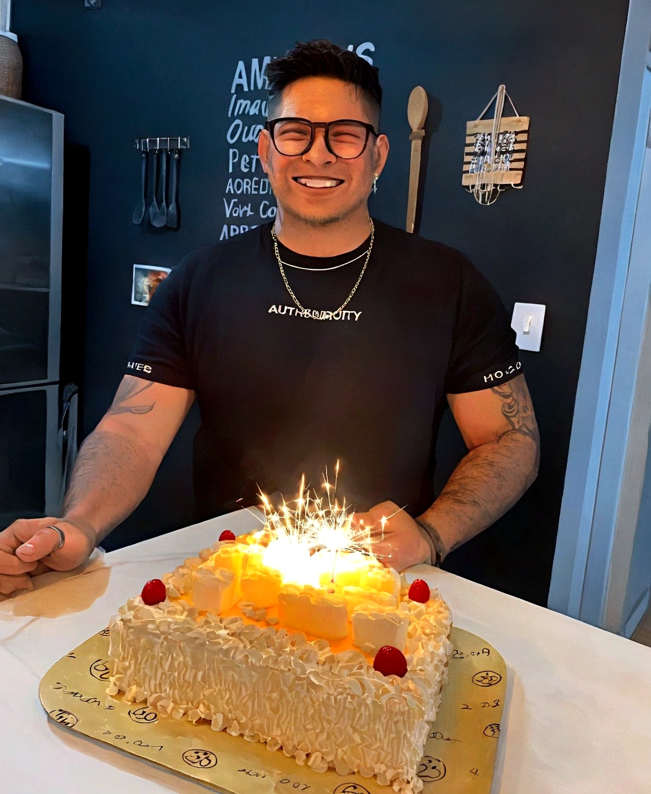 smiling man in glasses holding a birthday cake lit with candles, he is! about 30 years, he is about 30 years old, he is about 30 years, he is about 4 0 years old, he is about 40 years old, 29-years-old, 27 years old, he is about 2 , celebrating a birthday