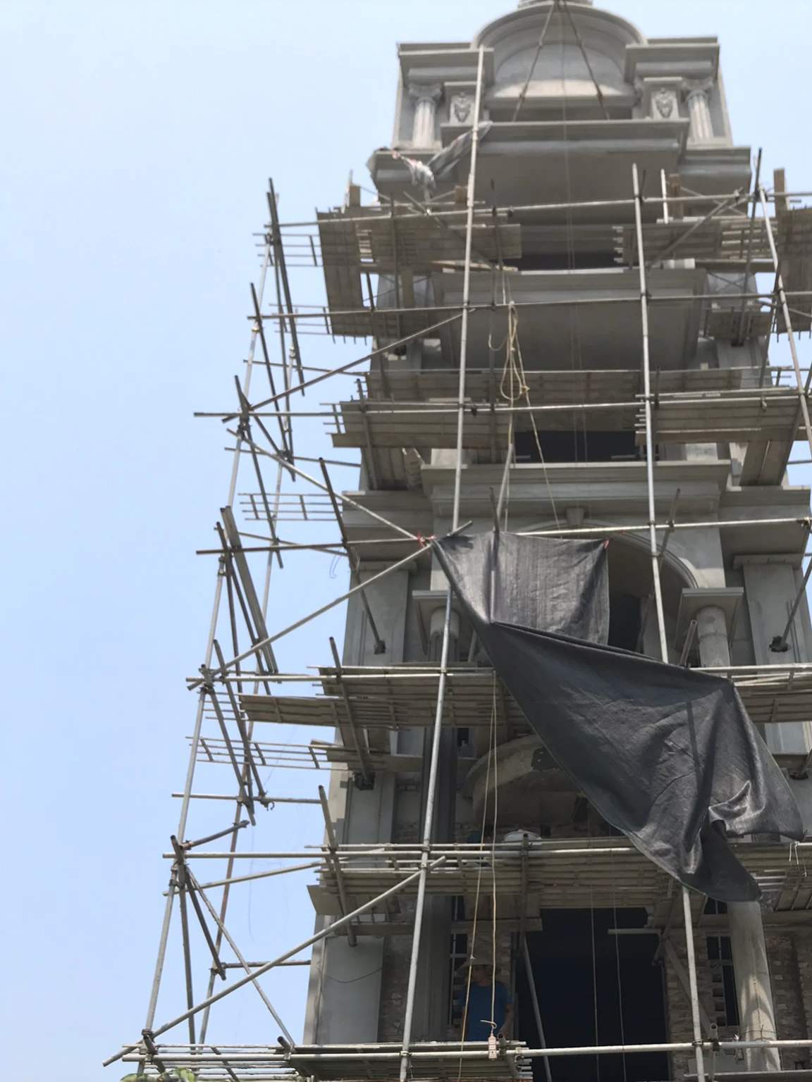arafed building with scaffolding and a clock tower with a flag on it, scaffolding collapsing, the building is a skyscraper, scaffolding, view from ground level, big poor building, building facing, the photo shows a large, viewed from the ground, view from bottom, tall thin build, view from ground, view from bottom to top, leaked image