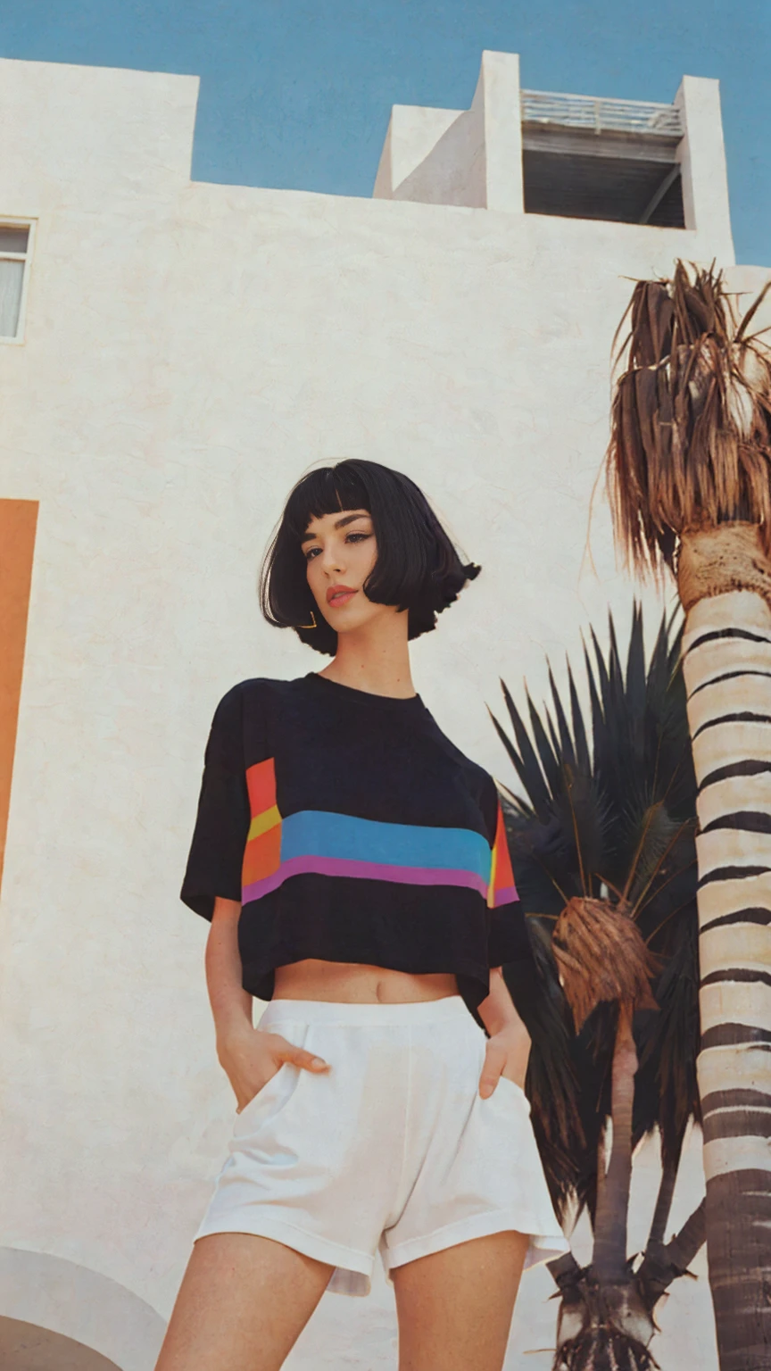 Best Quality,Masterpiece,Ultra High Resolution,(Realisticity:1.4),Original Photo, 1Girl, light leak,dark intens shadow,wear (blank white untucked t-shirt),black bob hairstyles background (80's mondrian architecture colourful motel),palm trees,sunny,summer, los Angles vibes,(from below:1.2), (realistic:1.1), (surreal:1.2), (very detailed:1.1)