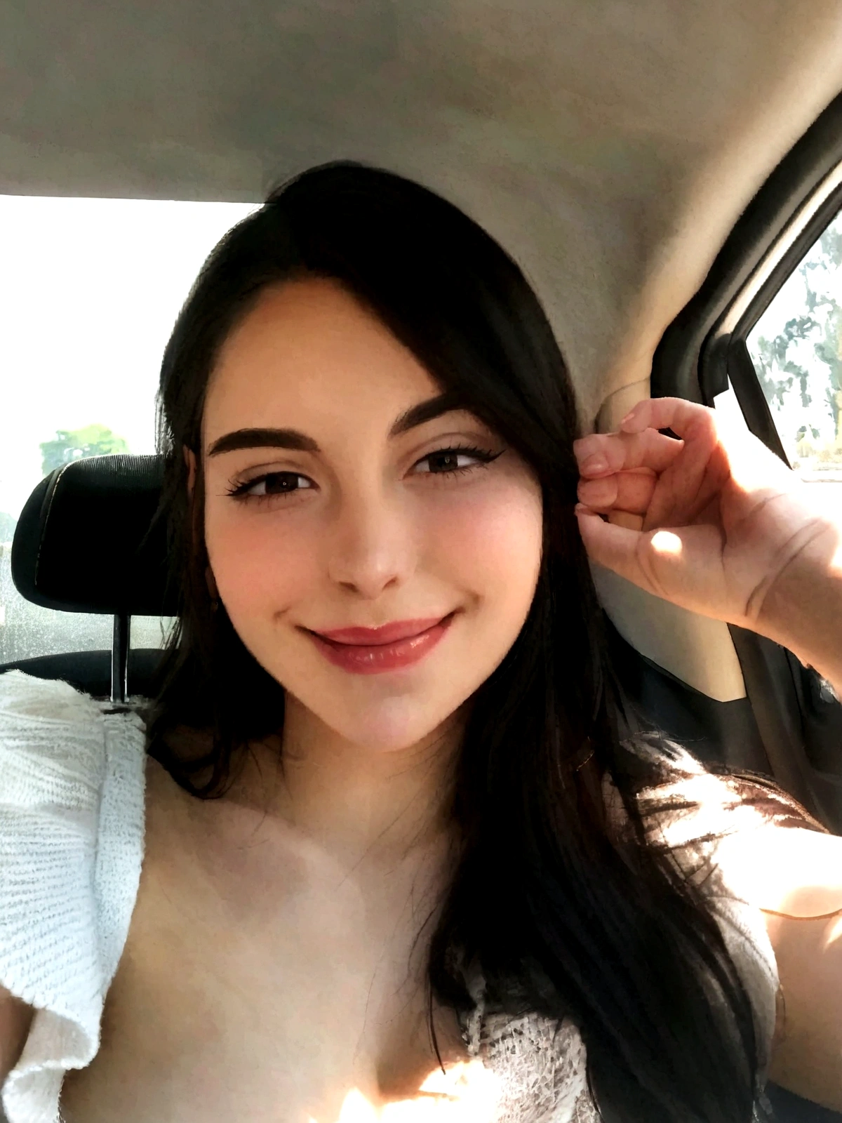 Woman with dark hair, fair skin, inside a car, small eyes, looking happy and serene