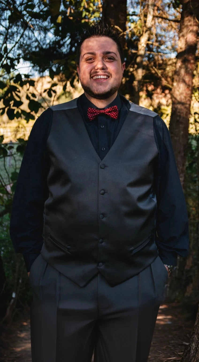 sharp man in vest and bow tie in front of a tree, formal portrait, black and red tuxedo, mid shot portrait, wearing a vest and a tie, Black Bow Tie, full body portrait shot, suit vest, detailed portrayal, groom, full body shot shot, wearing a tuxedo, formal outfit, formal suit, detailed professional photo
