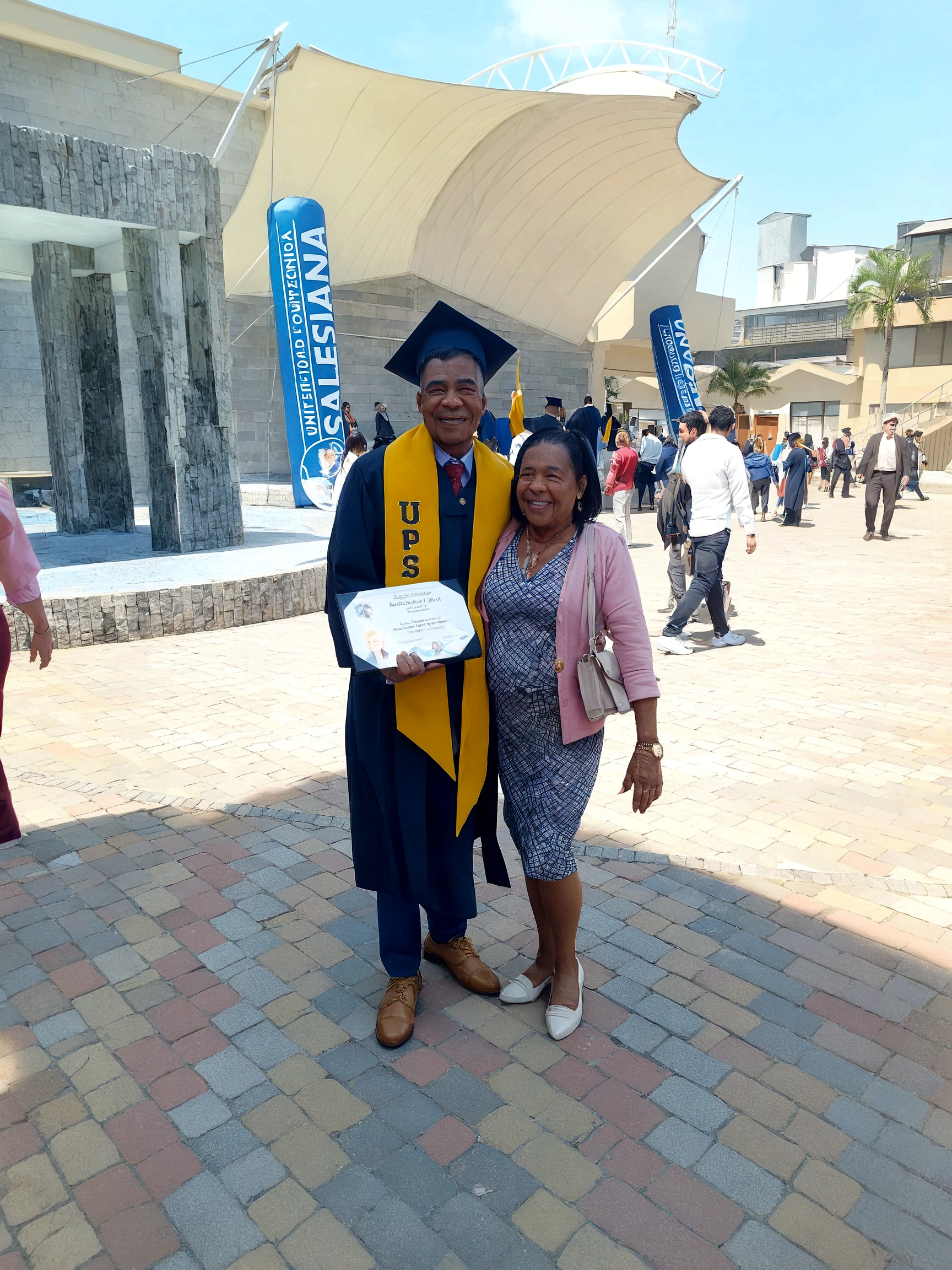 There are a man and a woman standing together in front of a building, album photo, Postgraduate, graduation photo, by Milton Menasco, 2 0 1 9, 2019, edited, photo taken in 2 0 2 0, wearing an academic gown, Lt. Bernie D&#39;Andrea, George Pemba, taken with the best dlsr camera