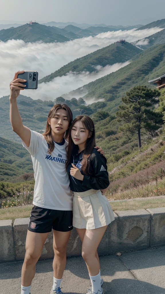 Lee Gahyeon from Korean k-pop group Dreamcatcher, taking a selfie with the South Korean soccer player Cho Guesung. She is blonde, he has dark hair. They are posing in front of a landscape. The landscape is the top of a mountain, with a bit of fog. It's an afternoon picture of their travel.